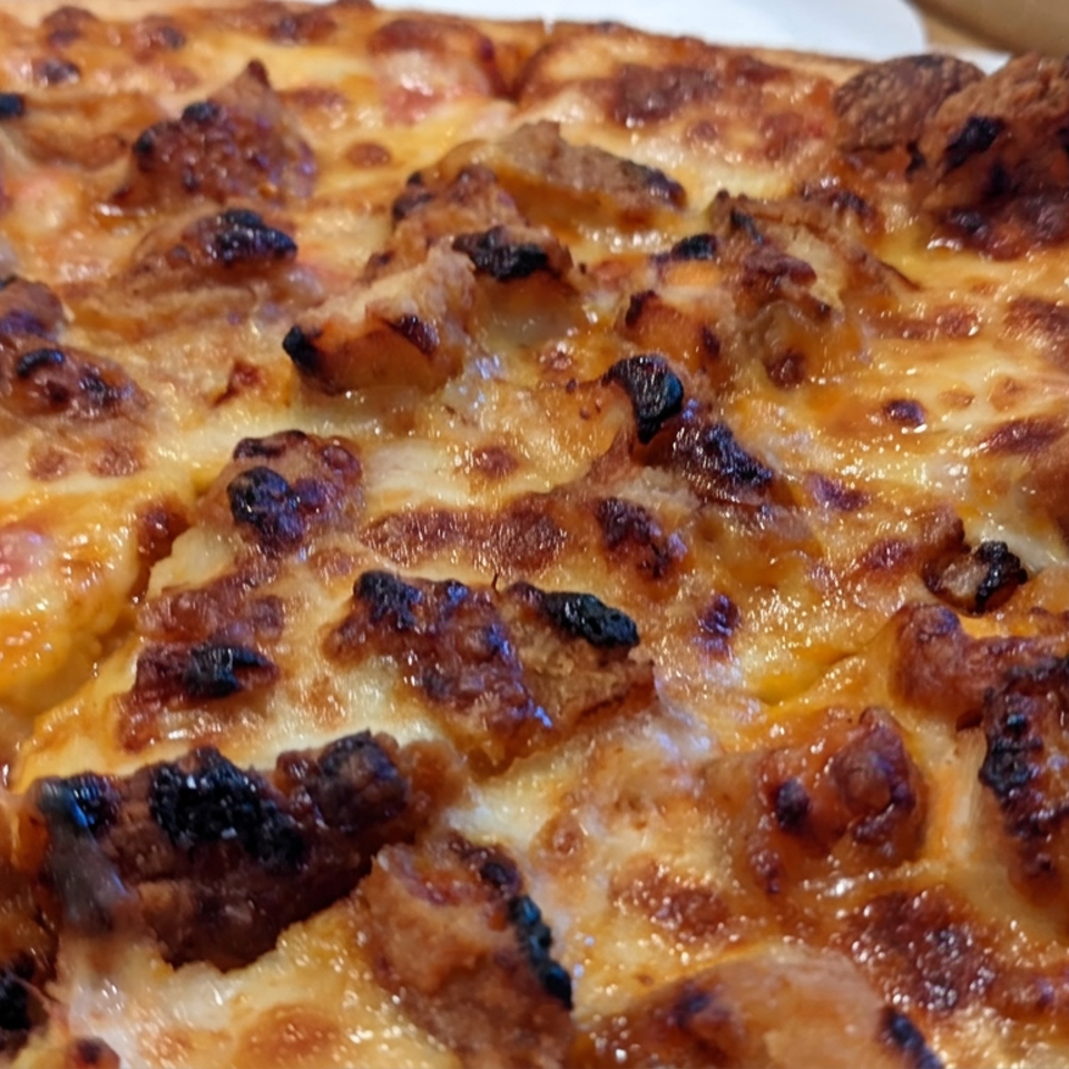 Close-up of a golden, cheese-covered pizza topped with browned sausage pieces and roasted toppings.